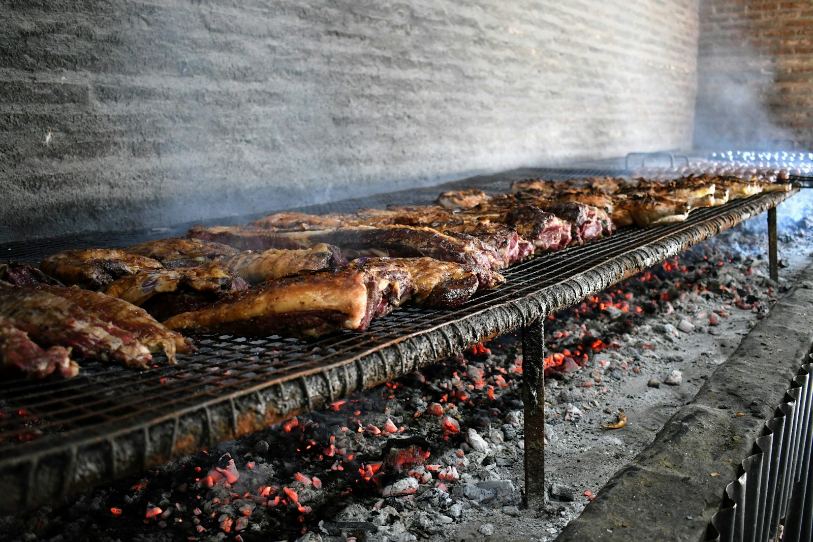Meat grilling slowly over glowing wood coals on a parrilla