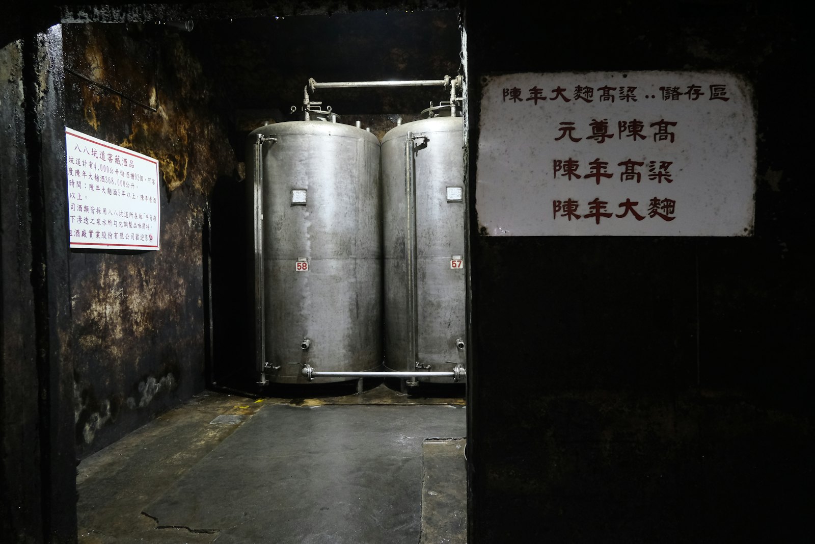 A row of stainless steel fermentation tanks in a dark winery interior
