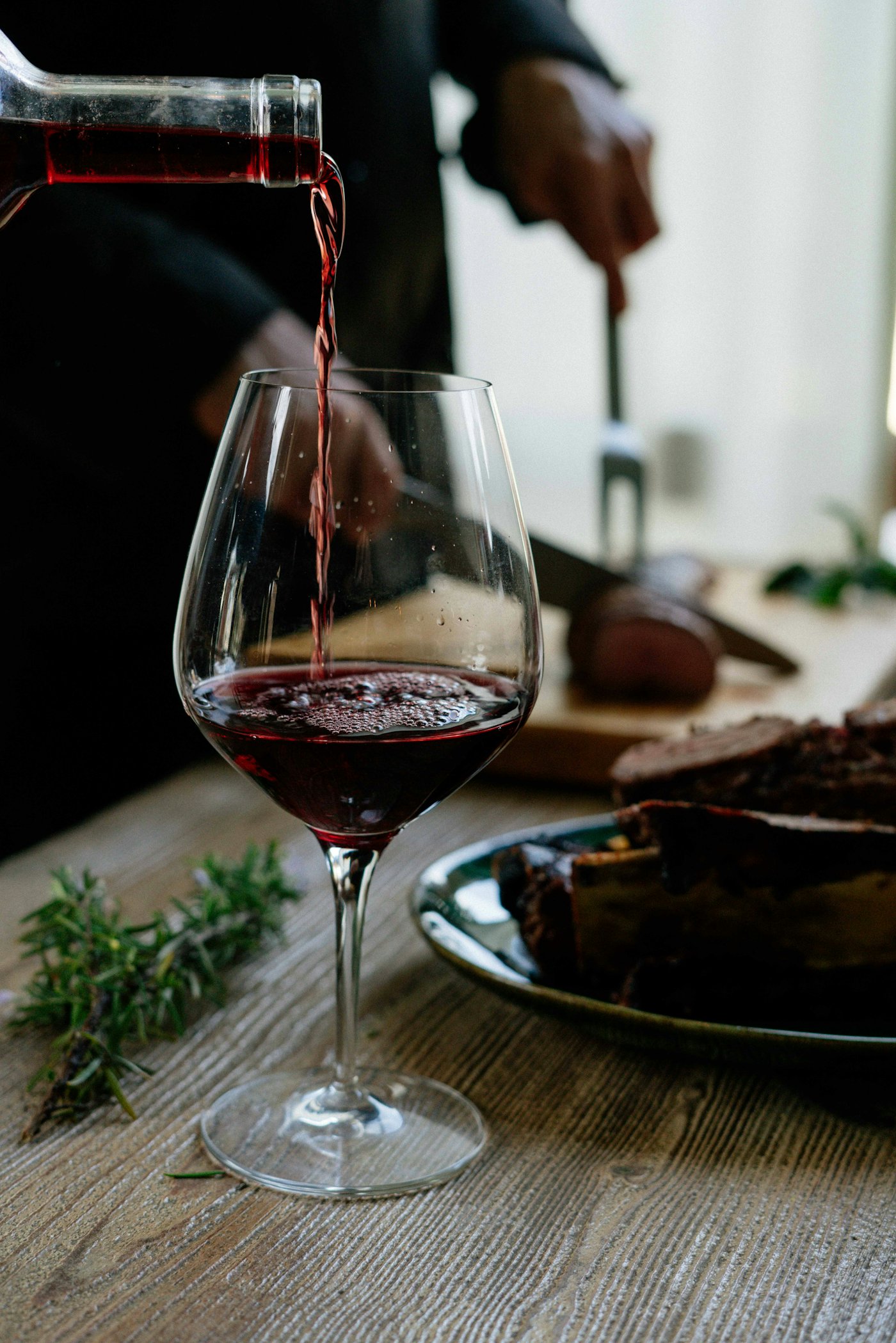 Deep ruby wine being poured into a glass decanter against warm soft light