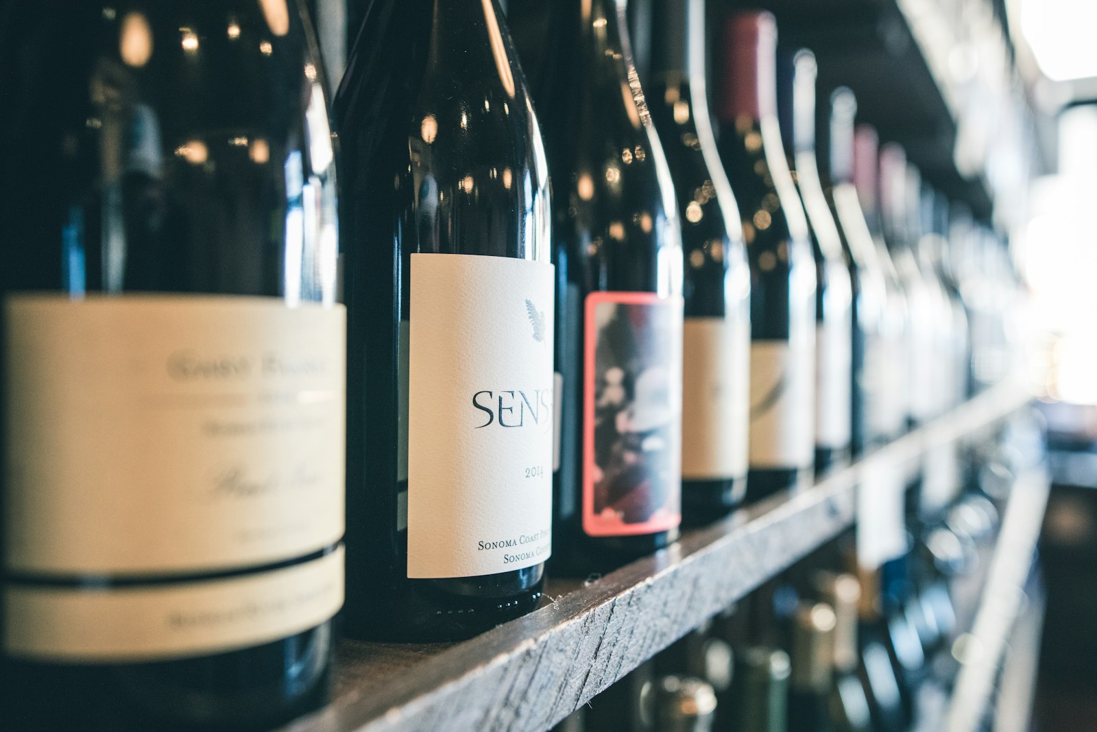 A row of wine bottles on a shelf, labels in focus under dramatic side-light
